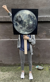 woman with a raised fist holding the moon painted on placard in front of her